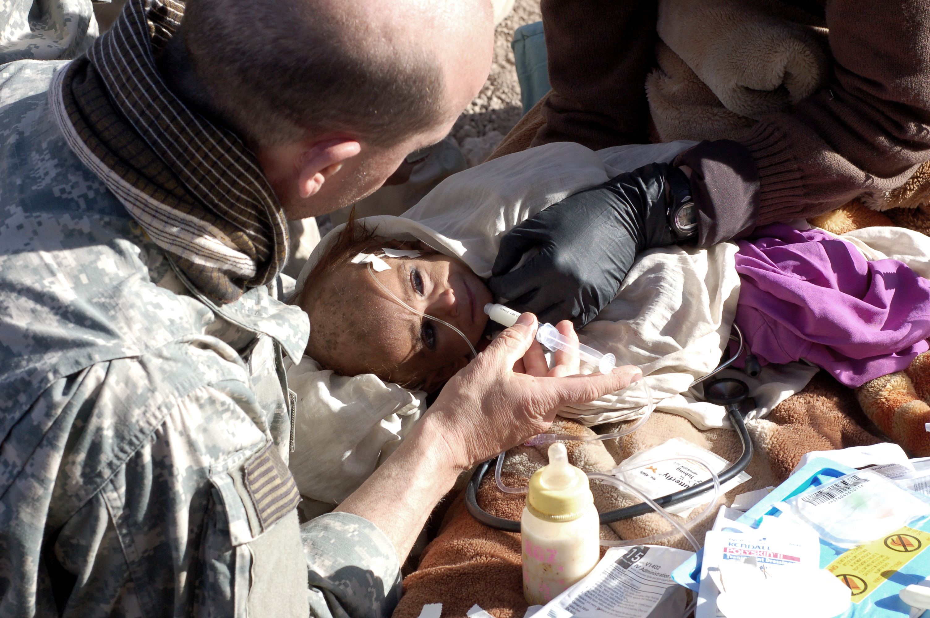 A U.S. Army medic tries to feed an 18-month gold Afghan girl using a syringe. She weighs approximately 14 pounds and is too weak to eat. 